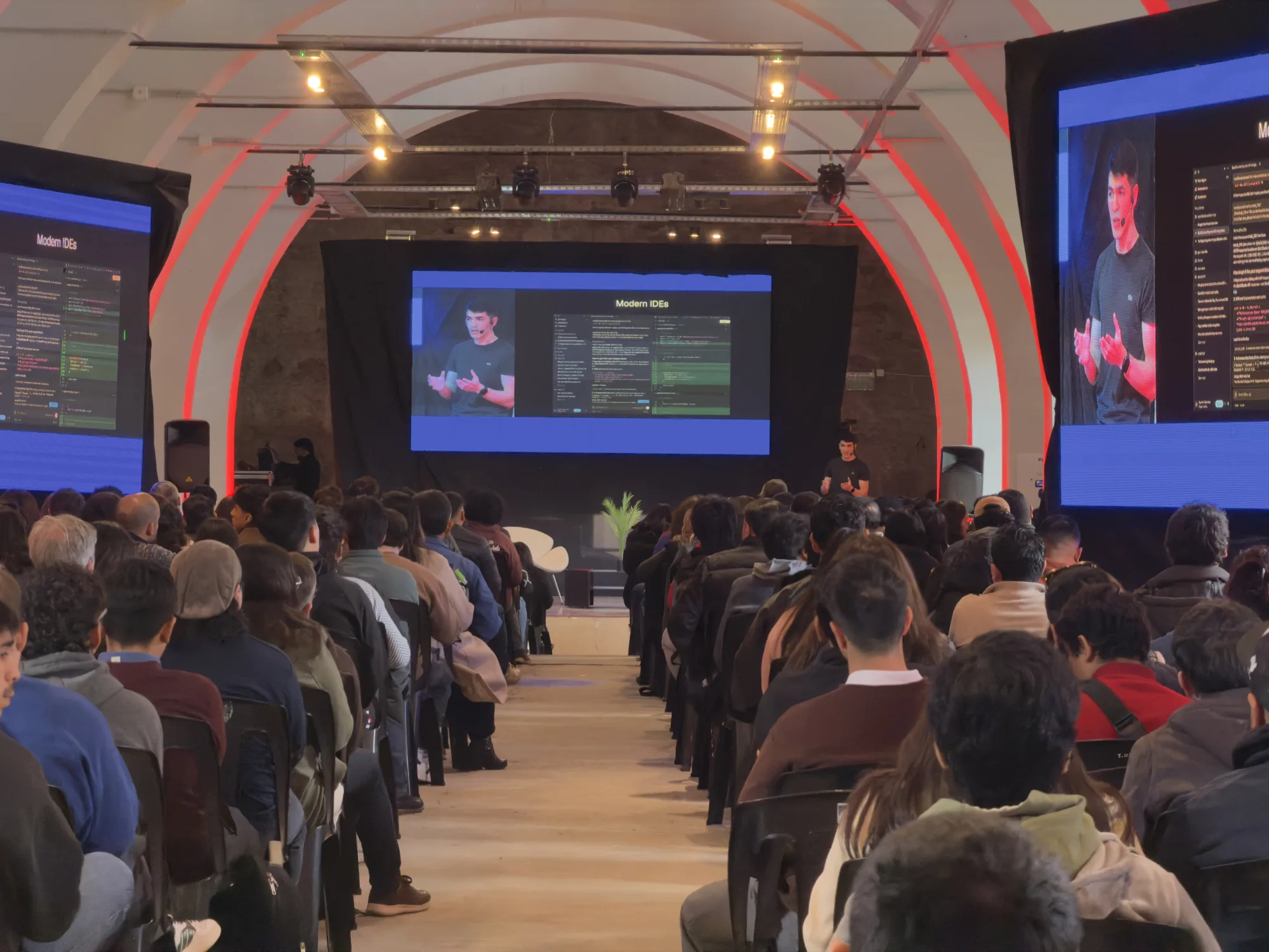 Agustín Sánchez giving a talk on stage, next to a slide reading "Agentic Software".